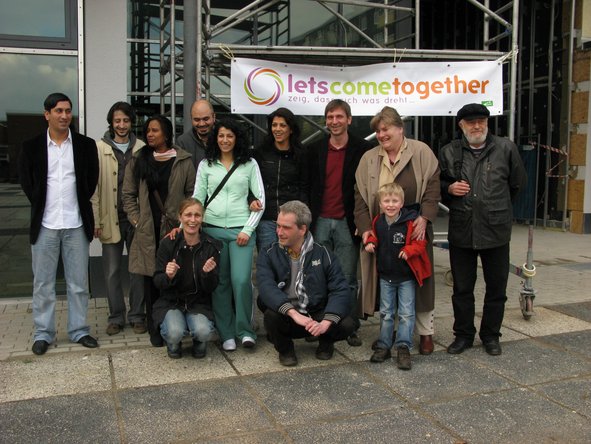 Eine Gruppe von Menschen steht und hockt vor einem Banner mit Schriftzug "Let's come together".