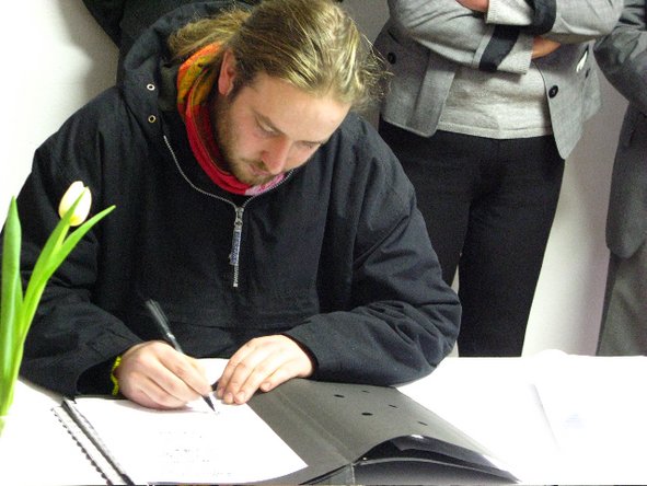 Philipp Unger sitzt an einem Tisch mit Dokumentenmappe und unterzeichnet einen Vertrag.